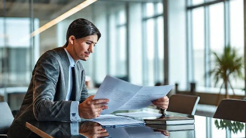 Photorealistic image of a business professional in a modern office setting, consulting with an expert (perhaps a lawyer or HR consultant) over a tablet, discussing complex regulatory documents. Professional, collaborative atmosphere, cinematic lighting, sharp focus on their interaction, depth of field, 8K.