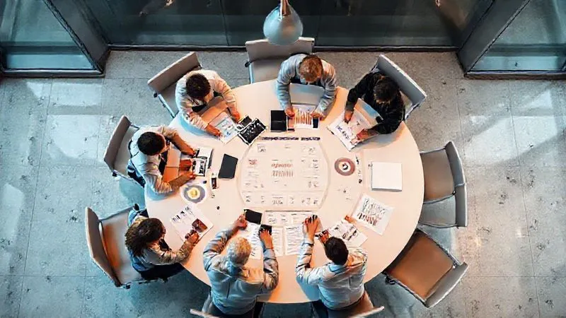 A photorealistic overhead shot of a diverse group of executives collaboratively working around a large circular table, with digital dashboards displaying compliance metrics and risk assessments, bathed in soft, professional office lighting, sharp focus on the team's interaction, depth of field blurring the modern office environment, 8K, professional photography. A photorealistic overhead shot of a diverse group of executives collaboratively working around a large circular table, with digital dashboards displaying compliance metrics and risk assessments, bathed in soft, professional office lighting, sharp focus on the team's interaction, depth of field blurring the modern office environment, 8K, professional photography.