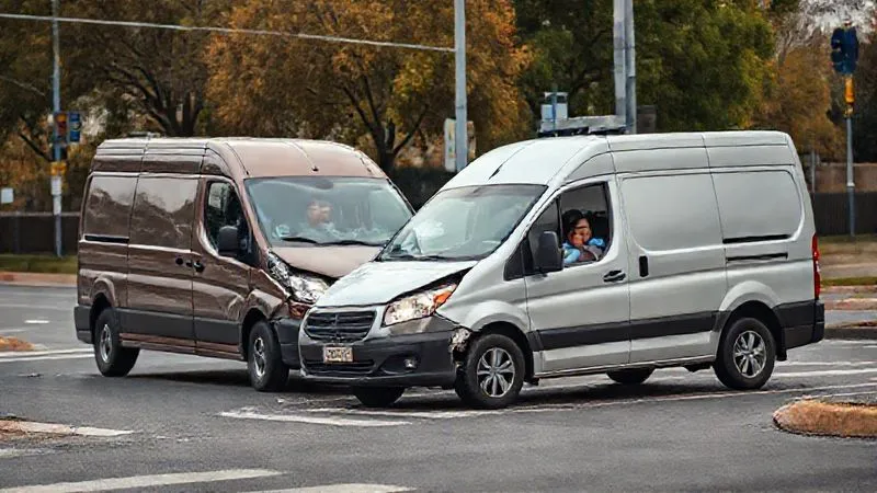Photorealistic, professional photography of a minor fender bender involving a commercial van and a passenger car at a street intersection. The focus is on the damage and the worried expressions of the drivers exchanging information. 8K, cinematic lighting, sharp focus, depth of field, shot on a high-end DSLR. No visible logos or text.